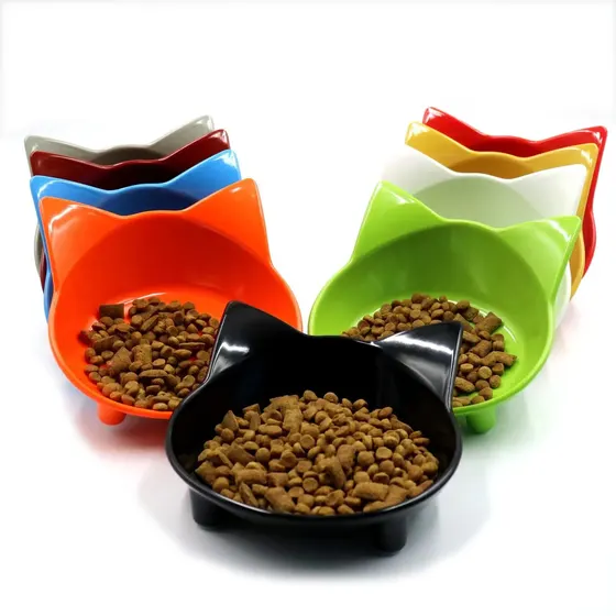 Multiple colorful cat-shaped ceramic bowls filled with dry pet food arranged on a white background