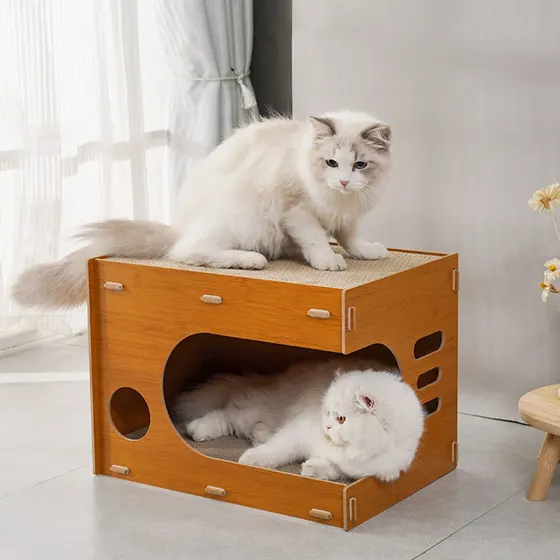 Two fluffy white cats resting on and inside a wooden cat house with a scratching pad on top.