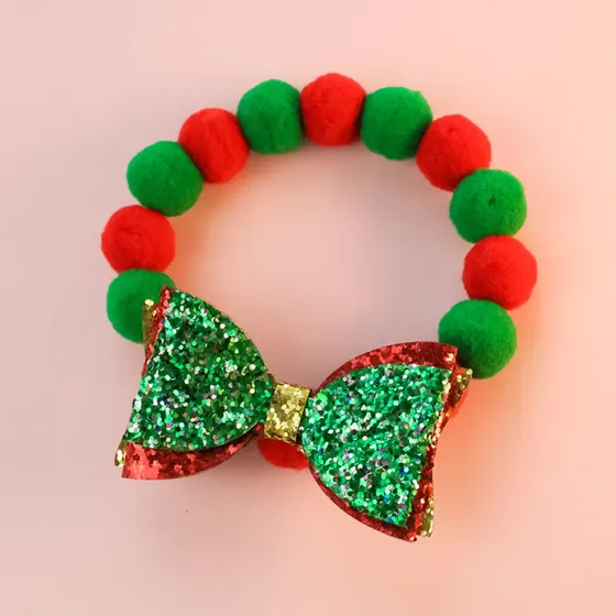Christmas headband featuring red and green pom-poms and a glittery sequin bow on a pink background.