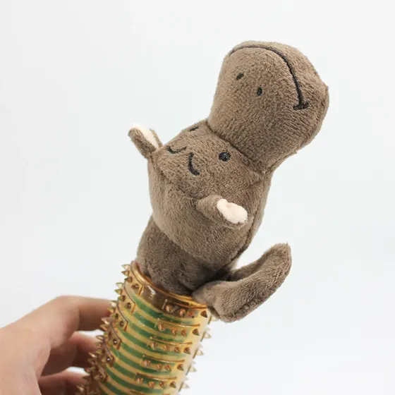 A hand holding a brown plush toy with a smiley face attached to a green and gold studded tube.