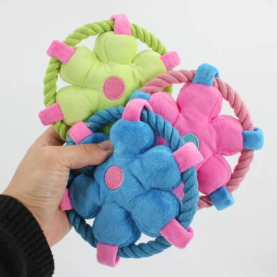 A hand holding three plush flower-shaped dog toys with attached rope rings in green, pink, and blue.
