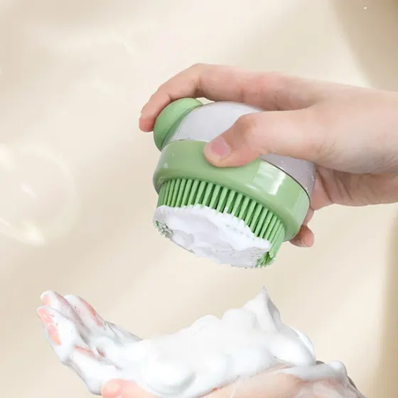 Hand holding a green and white silicone soap dispenser brush dispensing foam onto a palm.