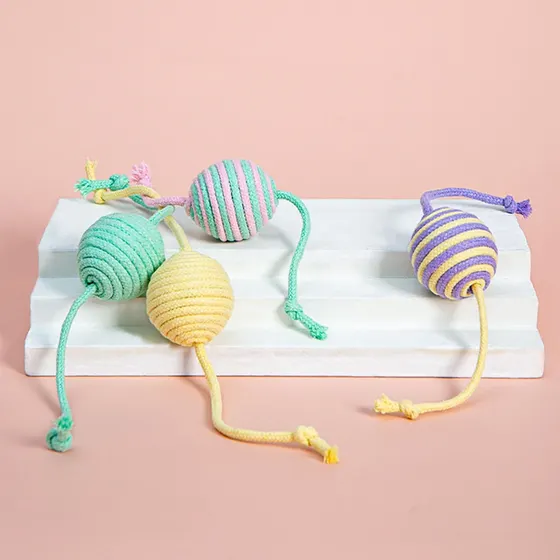 Four colorful braided cotton rope balls with strings arranged on a white wooden block against a pink background.