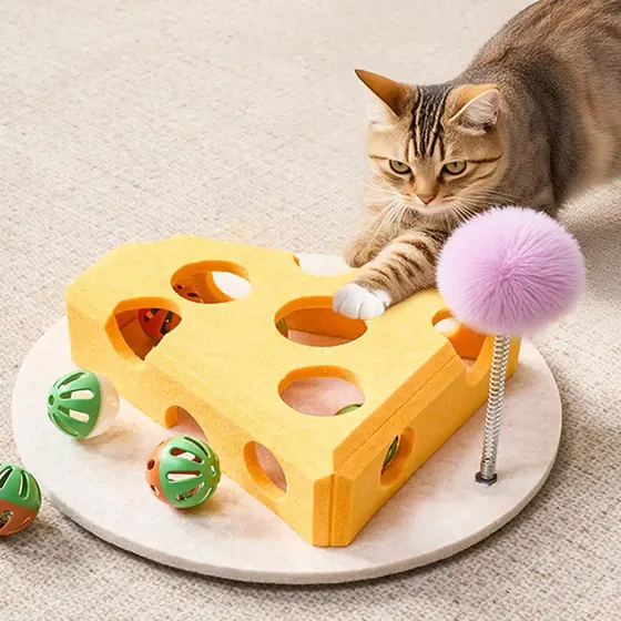 Tabby cat playing with a yellow cheese-shaped interactive puzzle toy featuring holes, balls, and a feather wand.