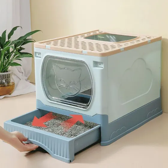 A hand pulls a tray of cat litter from a beige and blue enclosed litter box with a clear door.