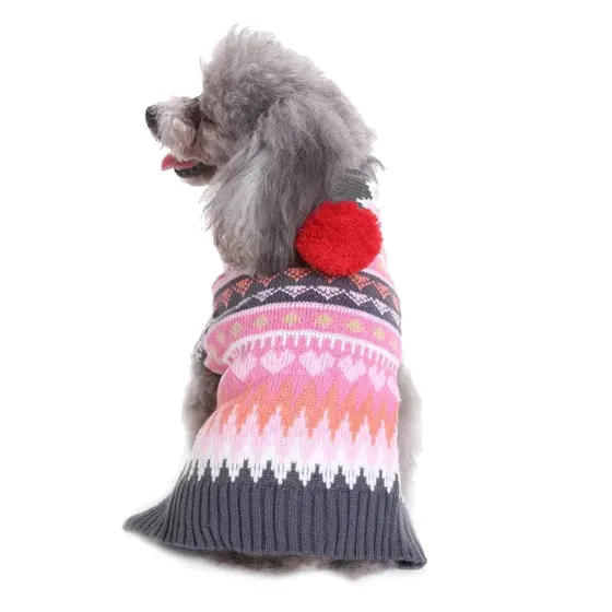 Grey poodle wearing a pink and grey patterned knit sweater with a red pom-pom on the back