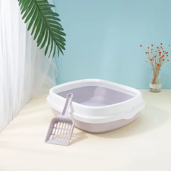A lavender and white plastic cat litter box with a matching scoop, set against a blue wall with decorative plants.