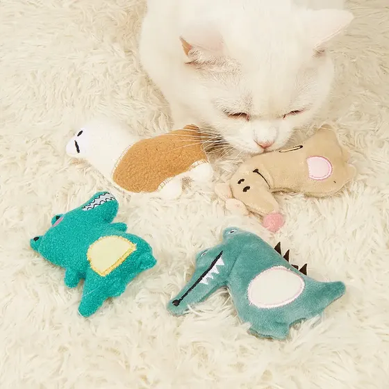 White cat sniffing plush dinosaur and animal catnip toys on a fluffy white rug.