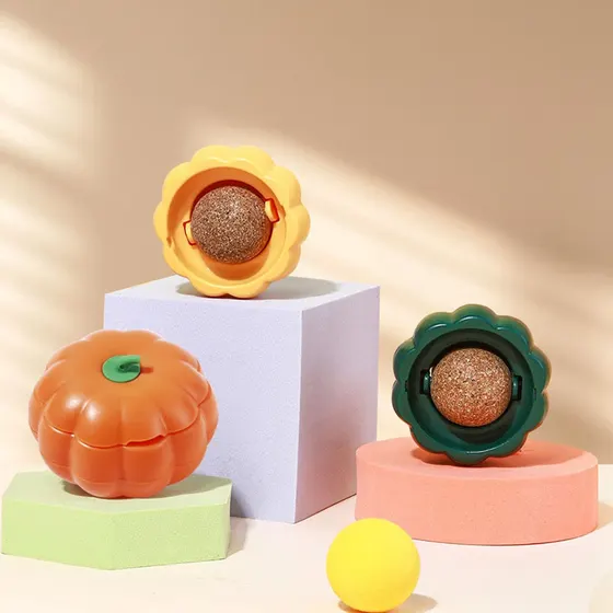 Three plastic pumpkin-shaped containers, two open to show a textured ball, on pastel pedestals.