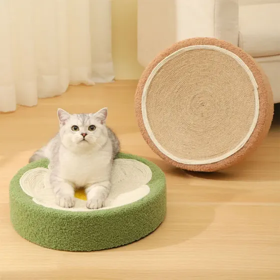 A silver and white cat resting on a green flower-shaped sisal cat bed with a matching round sisal scratcher behind.