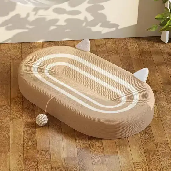 An oval cat scratcher mat with white concentric stripe patterns and attached ball toy sits on a wooden floor.