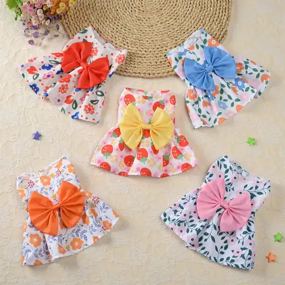 Five floral fabric bibs with large satin bows in red, blue, yellow, orange, and pink arranged on a beige surface.