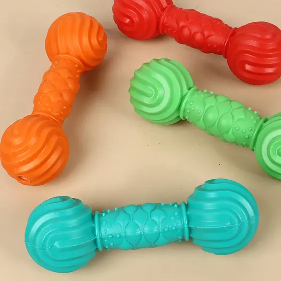 Four colorful dumbbell-shaped rubber dog chew toys with textured surfaces in orange, red, green, and blue