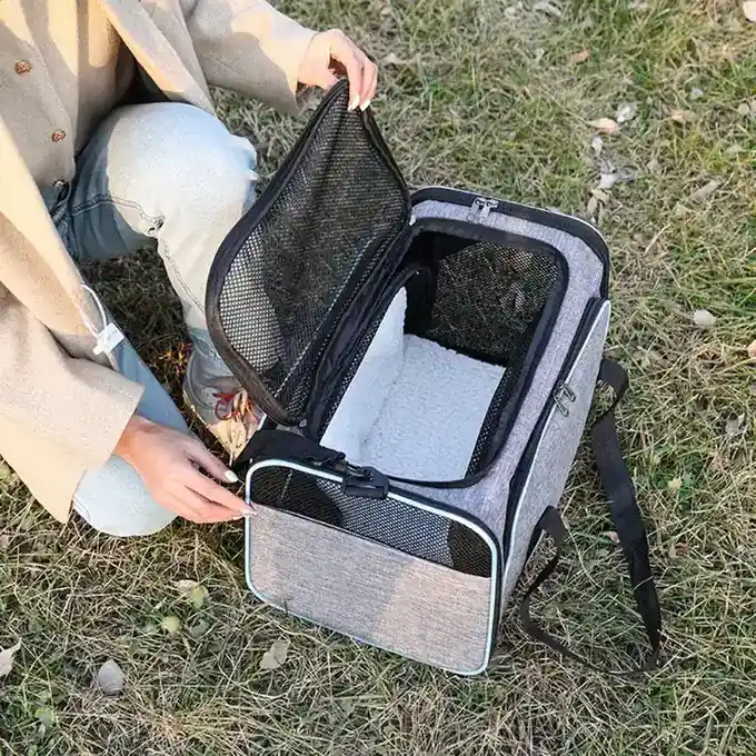 Open grey pet carrier bag with black mesh windows sitting on grass.