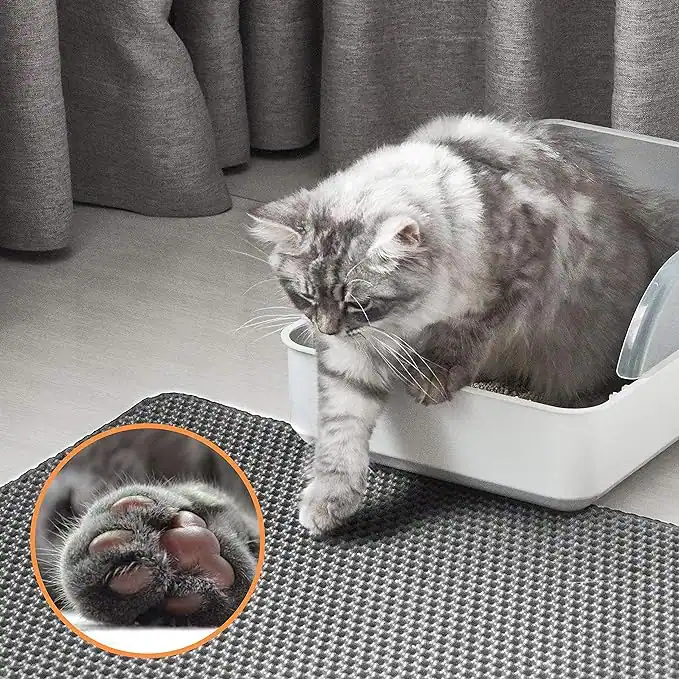 A fluffy grey cat steps out of a white litter box onto a textured grey honeycomb mat.