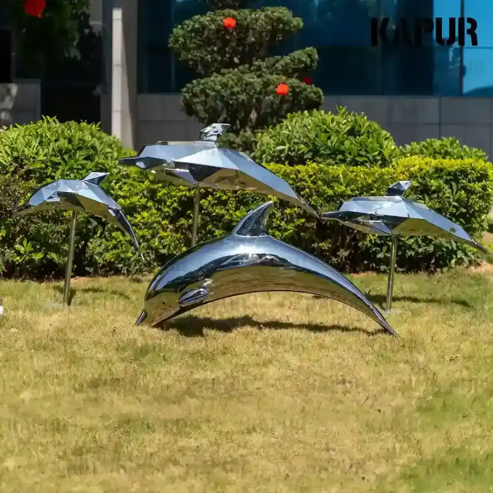 Polished stainless steel dolphin sculpture standing on a paved outdoor plaza, viewed from the front