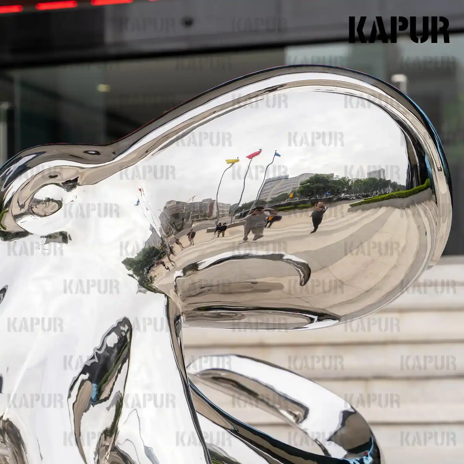 Polished stainless steel octopus sculpture with extended tentacles standing on a paved outdoor plaza