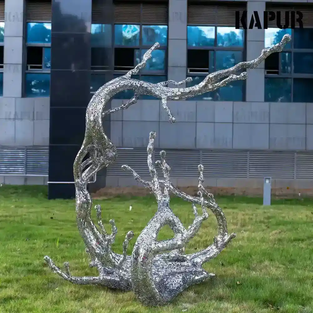 Abstract stainless steel sculpture shaped as a letter, water and flower standing on a paved outdoor plaza