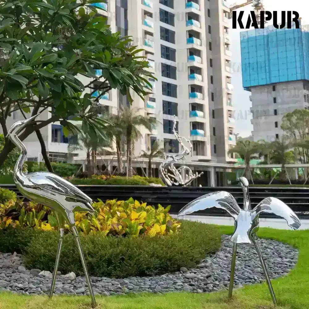 Polished stainless steel bird sculpture standing on a paved outdoor plaza, viewed from the front