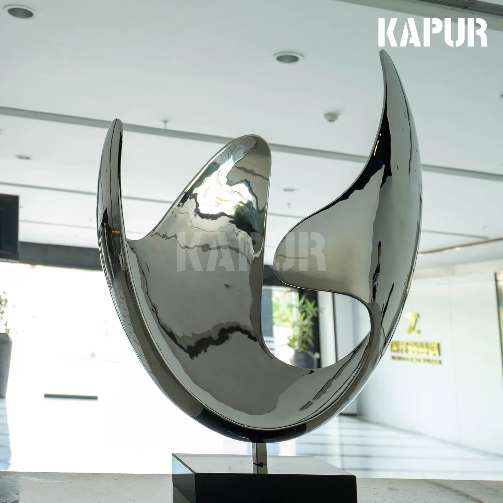 Modern abstract stainless steel sculpture in a reflective polished finish, standing in an open outdoor plaza