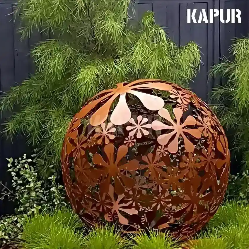 Corten steel garden metal ball sculpture standing in a natural outdoor garden setting with plants and stone pathways