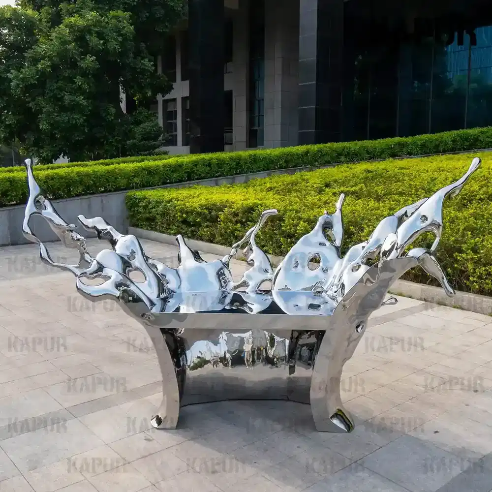Second view of the stainless steel water splash table sculpture showing the curved reflective surface and water flow pattern