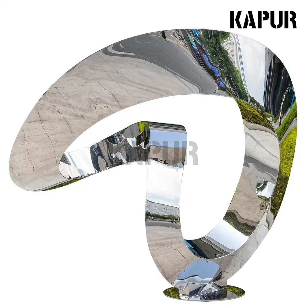 Polished stainless steel Möbius ring sculpture standing on a paved outdoor plaza, reflecting the sky and surrounding architecture