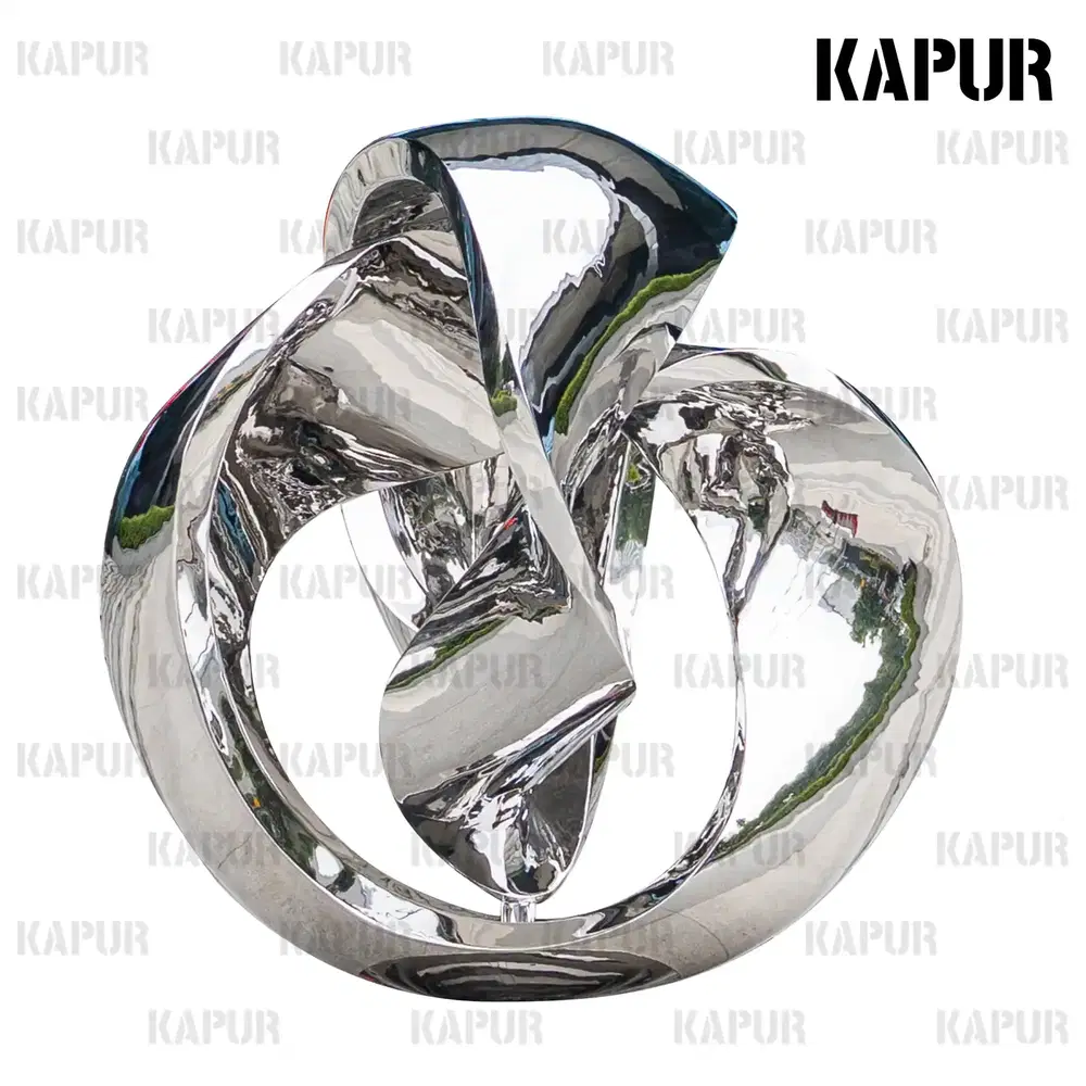 Polished stainless steel Möbius ring shaped ball sculpture standing on a paved outdoor plaza, reflecting the sky and surrounding architecture