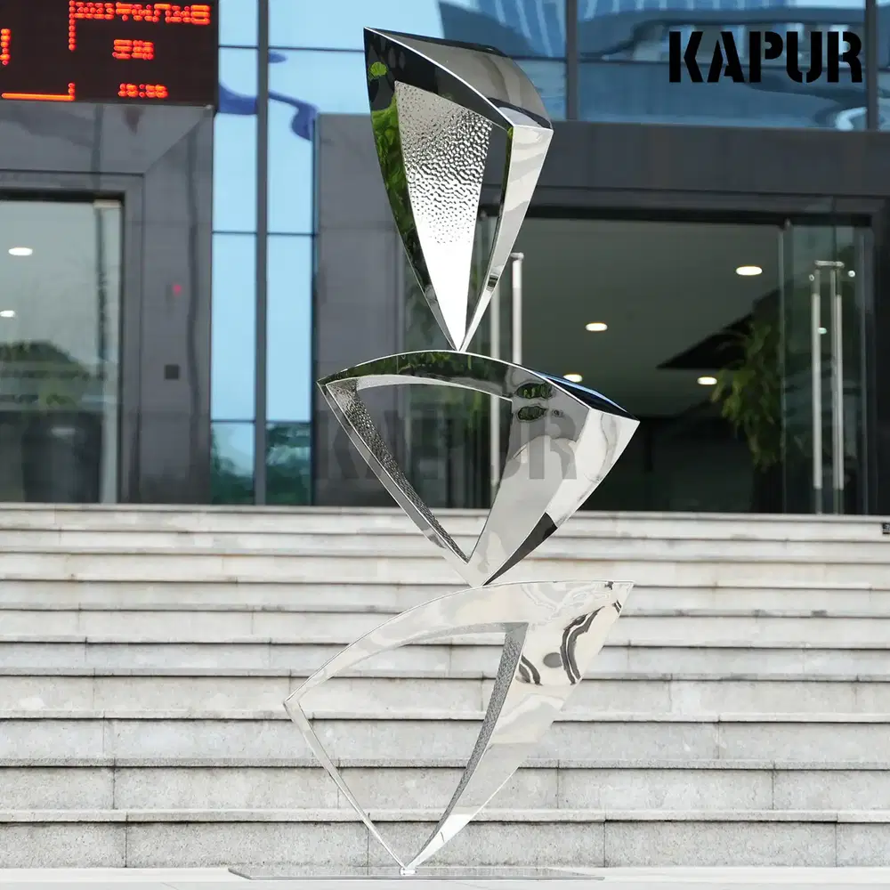 Modern abstract stainless steel sculpture in a polished finish standing in an outdoor garden setting