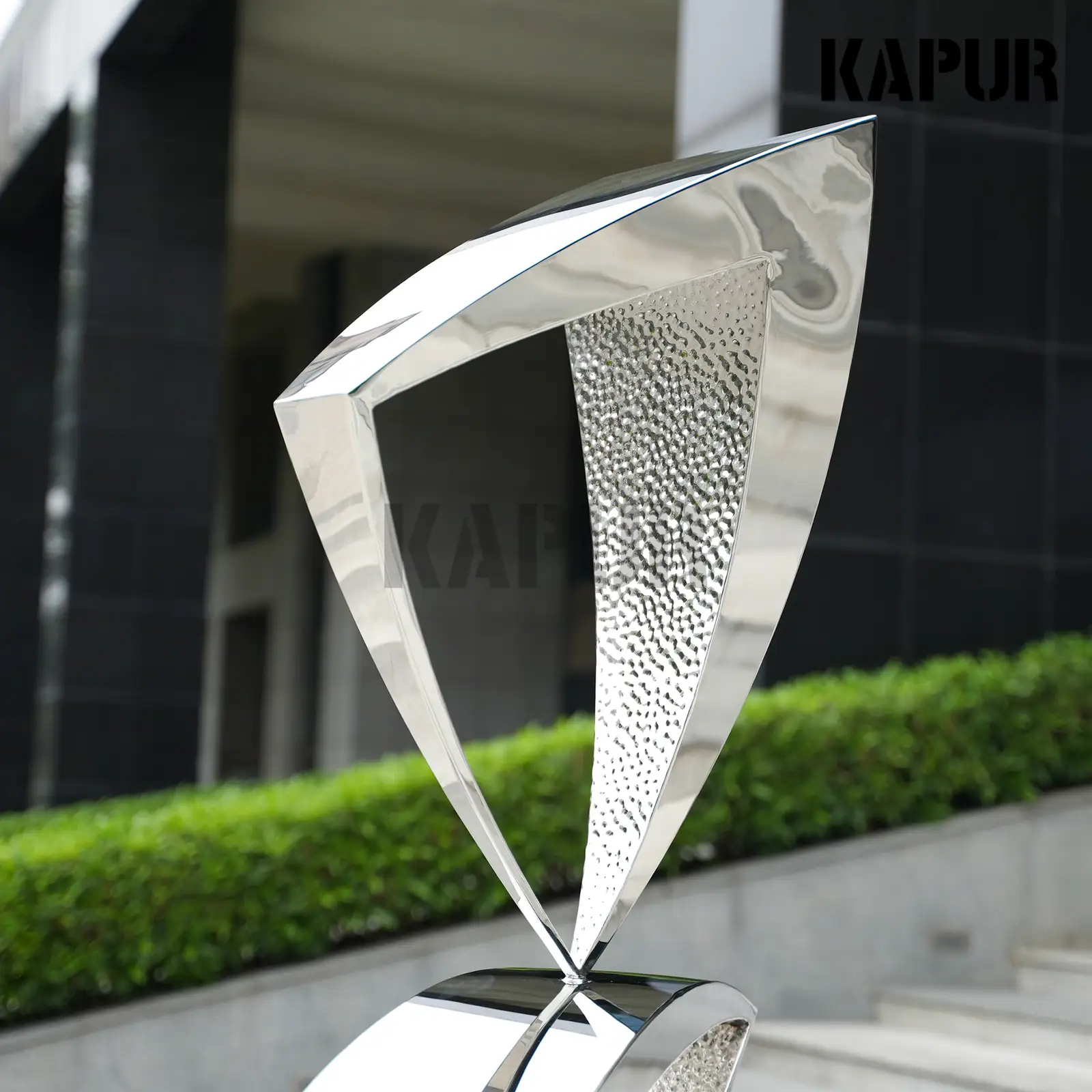 Second view of the modern stainless steel sculpture showing the reflective curved surface and welded seams