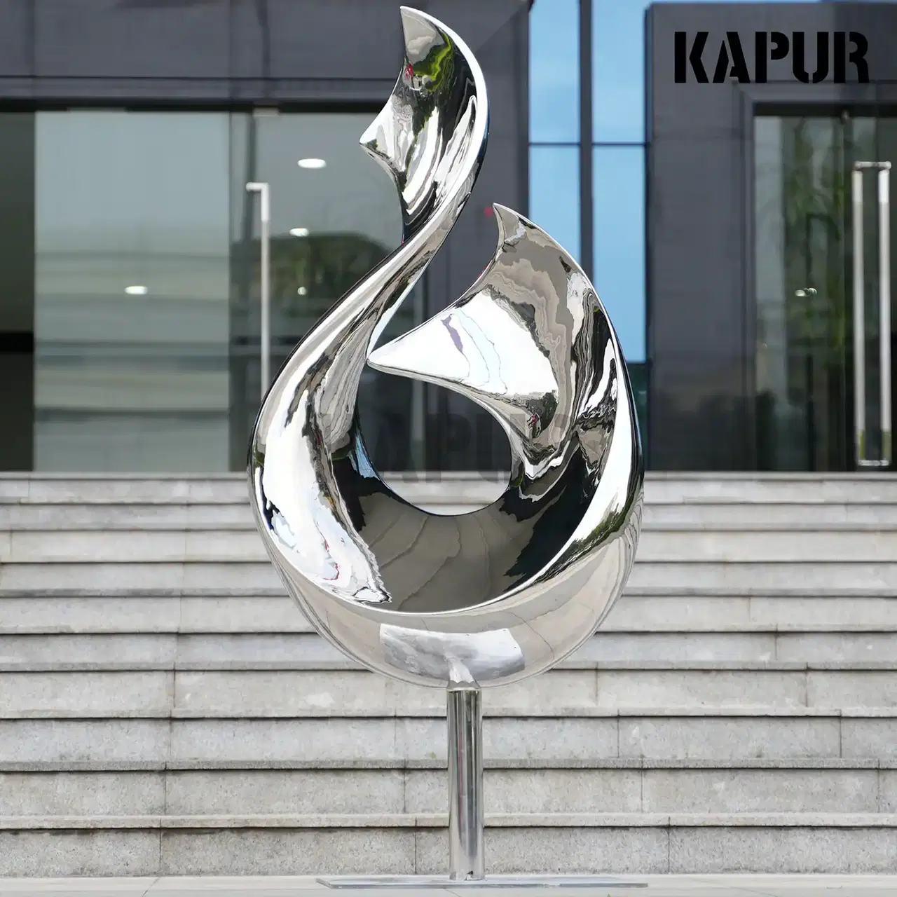 Polished stainless steel twisted ribbon sculpture standing on a paved outdoor plaza