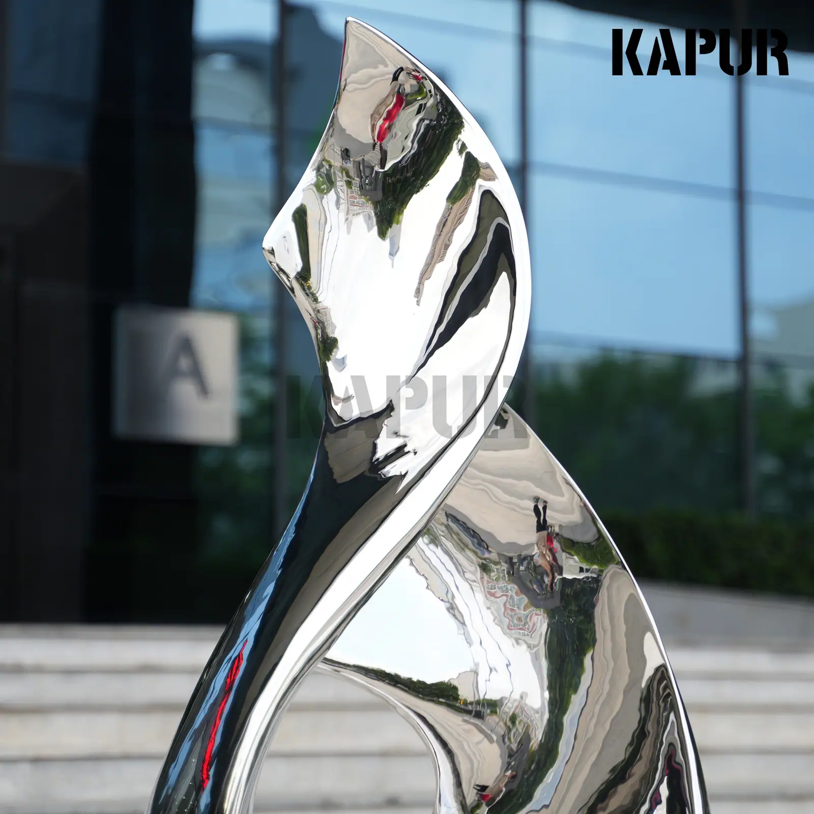Second view of the twisted stainless steel sculpture showing the curved reflective surface