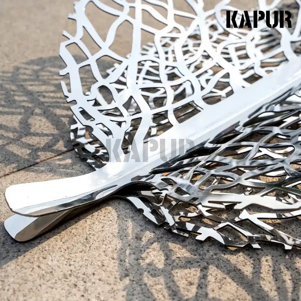 Second view of the leaf-shaped stainless steel sculpture showing the curved reflective surface from the side