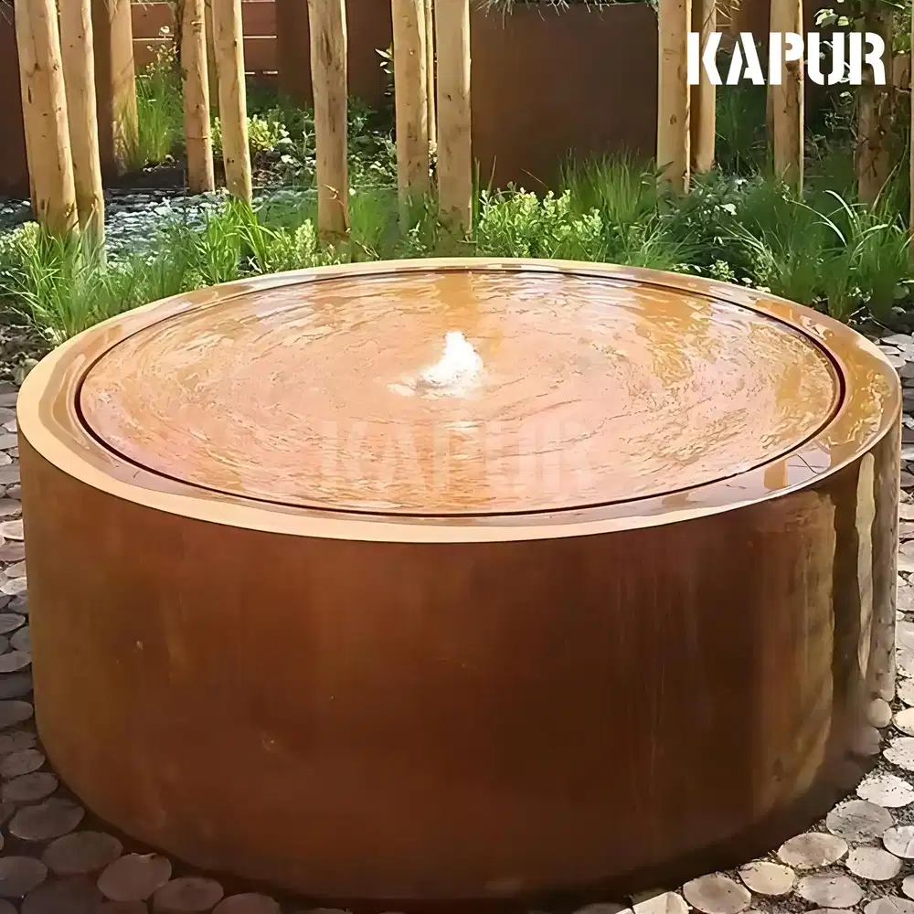 Round corten steel garden water table with a natural rust patina, placed in a garden setting with plants around it