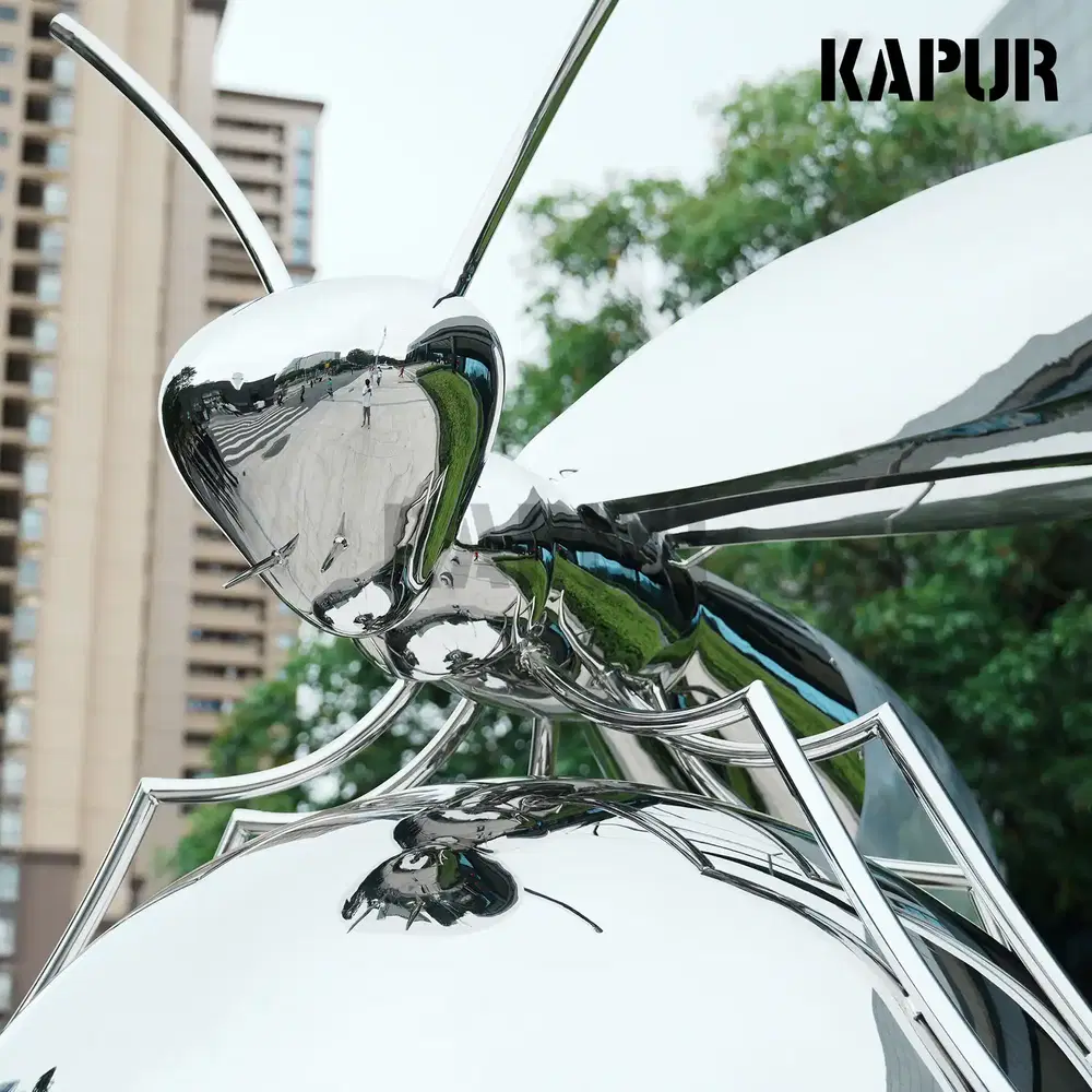 Second view of the stainless steel bee sculpture showing the reflective surface and curved wings