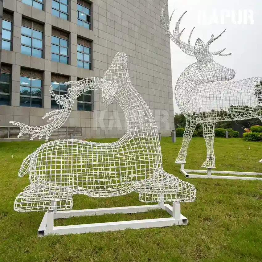Polished stainless steel wire deer sculpture standing in a modern garden setting with reflective surface catching sunlight