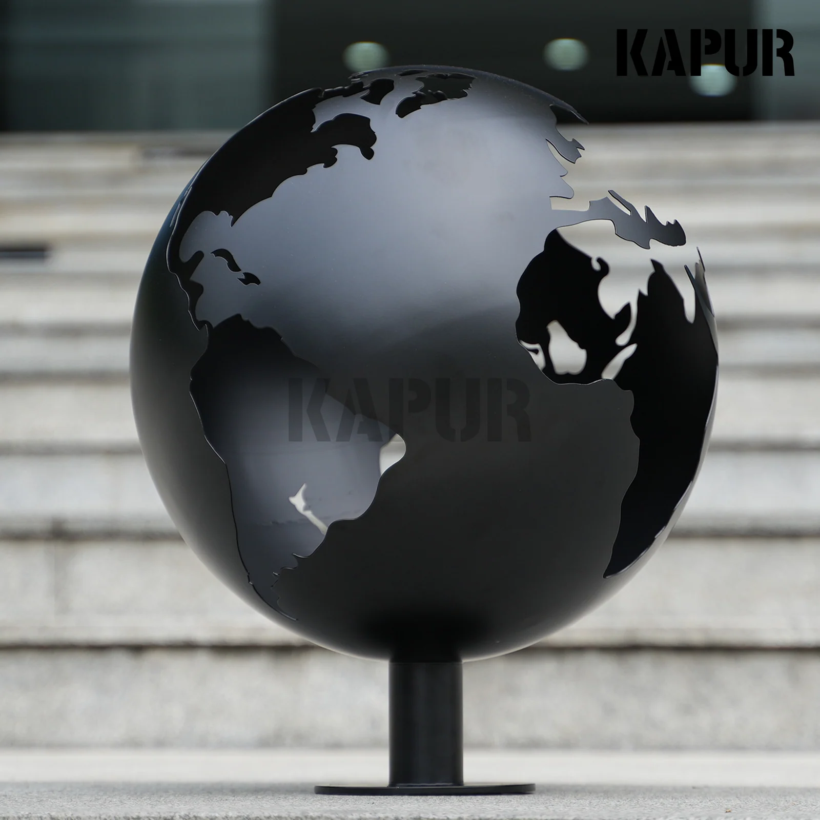 Black openwork stainless steel garden sculpture standing in a modern outdoor garden with reflective polished surface