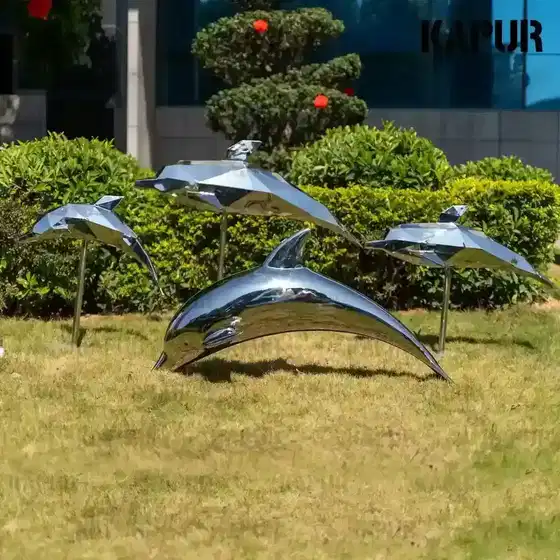 Polished stainless steel dolphin sculpture standing on a paved outdoor plaza, viewed from the front