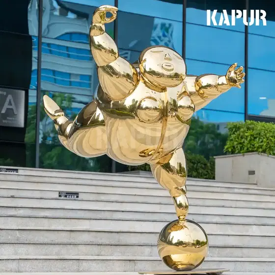 Abstract stainless steel sculpture of a dancing fat man standing on a paved outdoor plaza, reflective surface catching sunlight