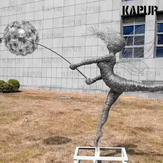 Art Deco stainless steel fairy dandelion sculpture standing on a paved outdoor plaza with reflective surface catching sunlight