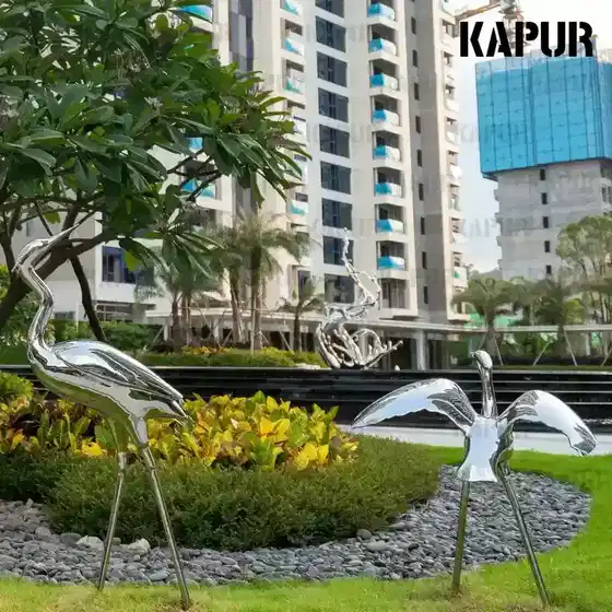 Polished stainless steel bird sculpture standing on a paved outdoor plaza, viewed from the front