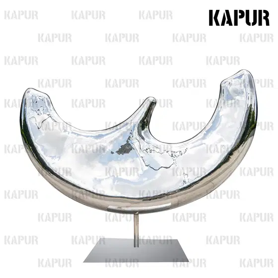Polished stainless steel moon-shaped sculpture standing on a paved city plaza with reflective surface catching sunlight