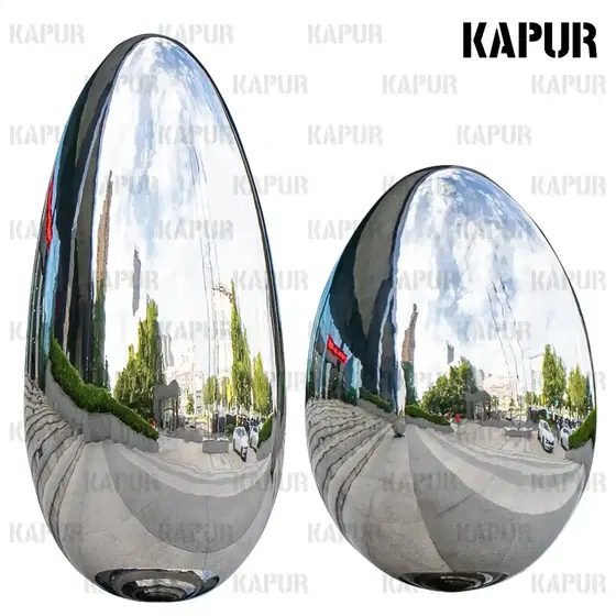 Egg-shaped oval stainless steel sculpture standing on a paved outdoor plaza with reflective surface