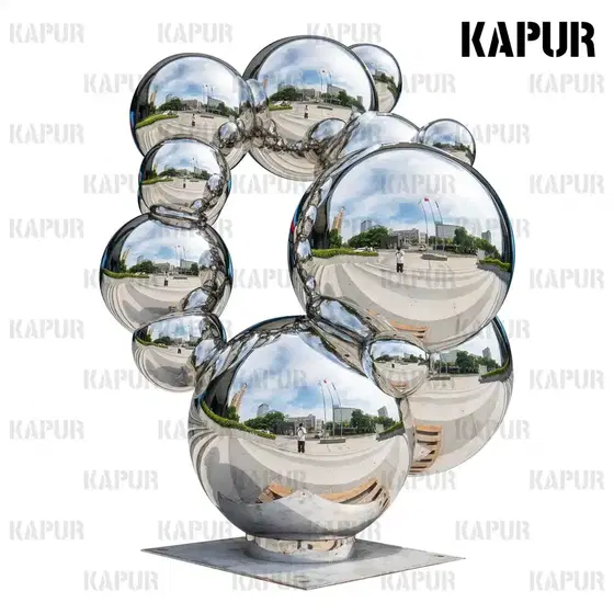 Large mirror-polished stainless steel sphere standing on a paved outdoor plaza, reflecting the sky and surrounding architecture