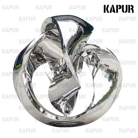 Polished stainless steel Möbius ring shaped ball sculpture standing on a paved outdoor plaza, reflecting the sky and surrounding architecture