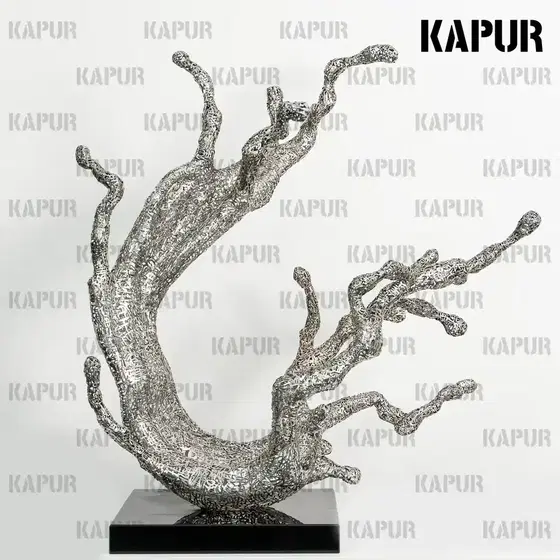 Polished stainless steel hollow wave sculpture standing on a paved outdoor plaza, reflecting the sky and surrounding architecture
