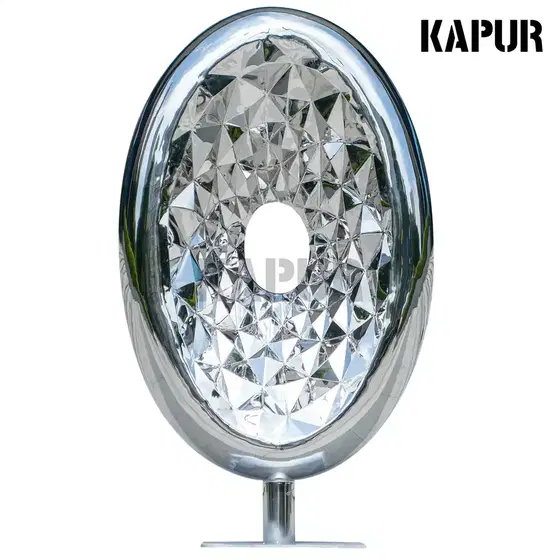 Polished stainless steel oval gemstone sculpture standing on a paved outdoor plaza, reflecting light and surrounding architecture