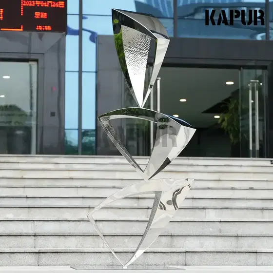 Modern abstract stainless steel sculpture in a polished finish standing in an outdoor garden setting