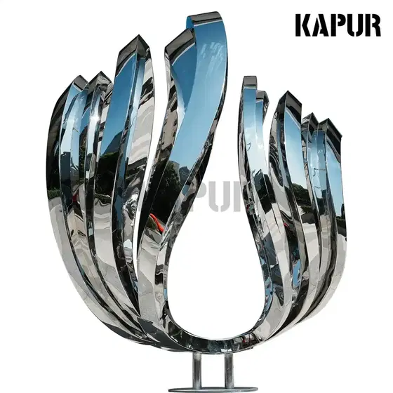 Polished stainless steel wave-wing sculpture standing on a paved outdoor plaza with reflective surface catching sunlight