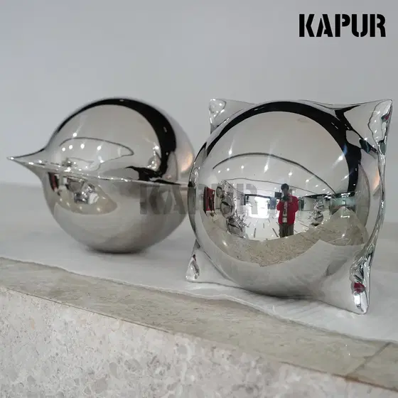 Mirror-polished stainless steel decorative ball standing on a paved outdoor plaza, reflecting sky and surrounding architecture